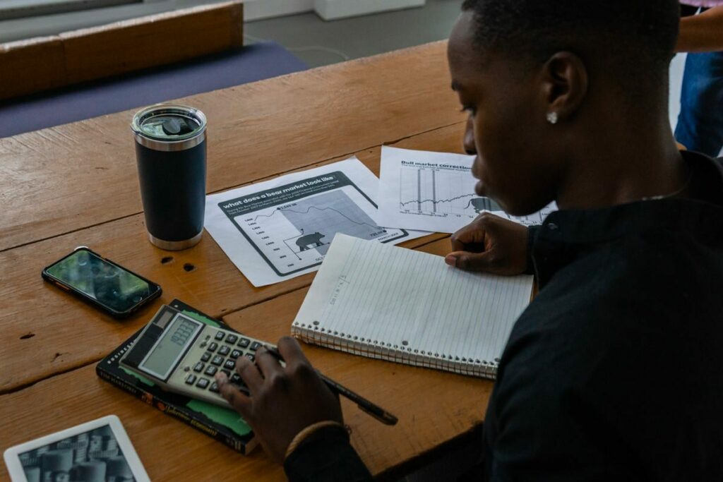 Young professional evaluating financial data using a calculator and notes.